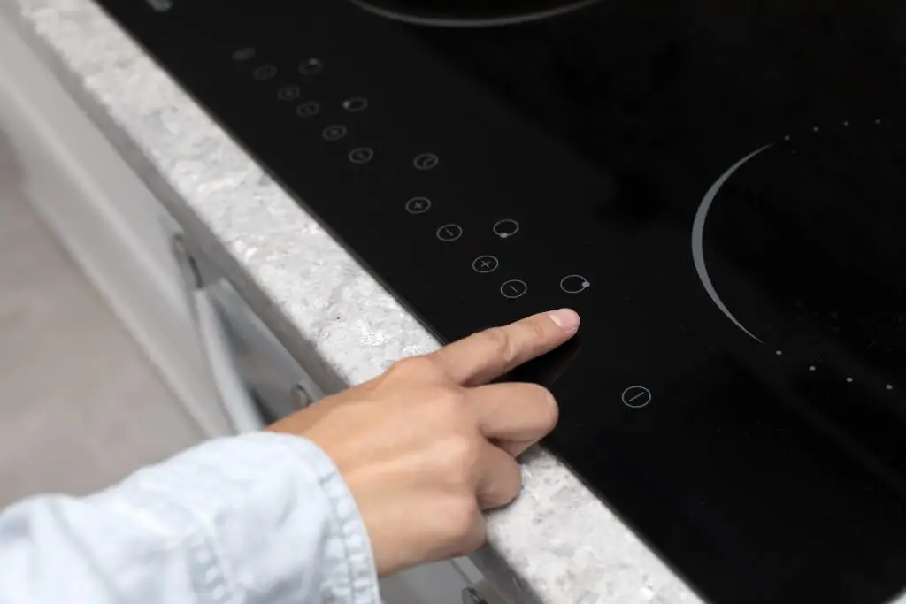 Woman adjusting temperature of black electric stove top burner, pressing start button on touch screen of cooker in kitchen, closeup