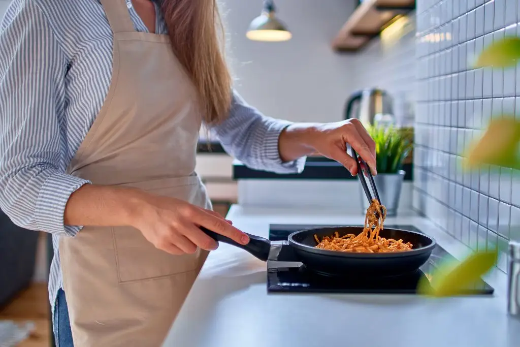Woman wearing apron preparing food in a frying pan on a hob