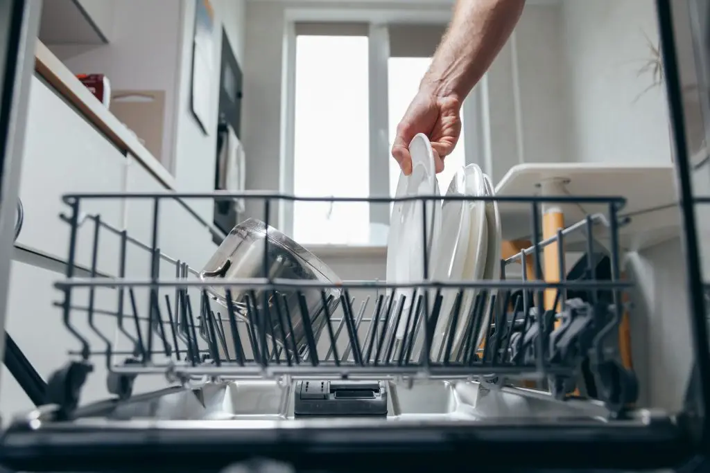 Male hand putting dirty plate in dishwasher, view from inside dishwasher. Household chores, man washing dishes