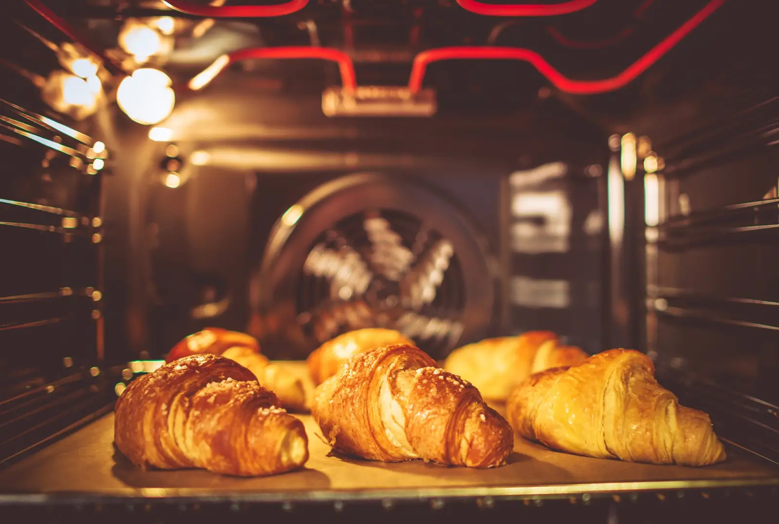 Croissants baking inside a fan-assisted oven — the top element browns the surface while circulated heat cooks the layers through evenly