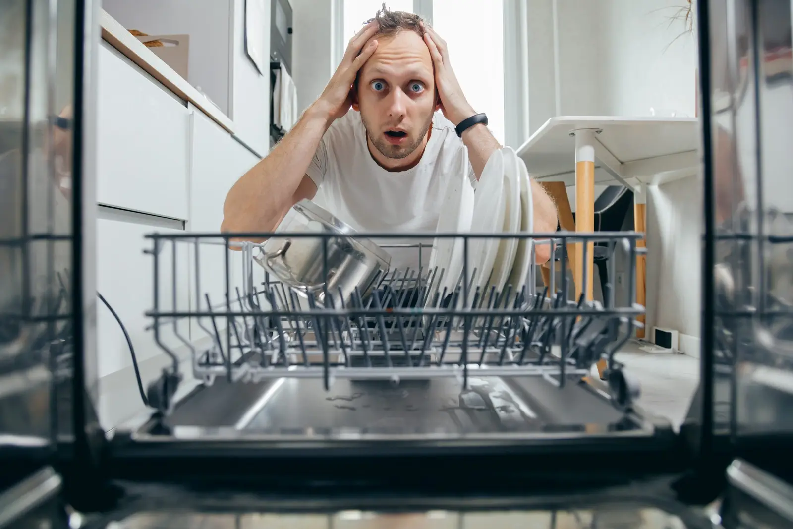 Frustrated man looking at dishes in an open dishwasher — dirty results often trace back to a tablet that did not dissolve during the cycle
