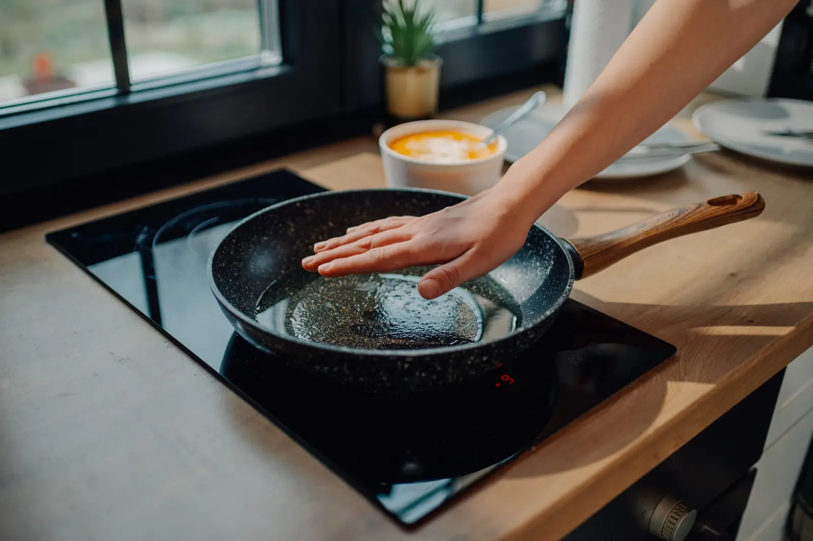 Hand checking the temperature of a frying pan on an induction hob