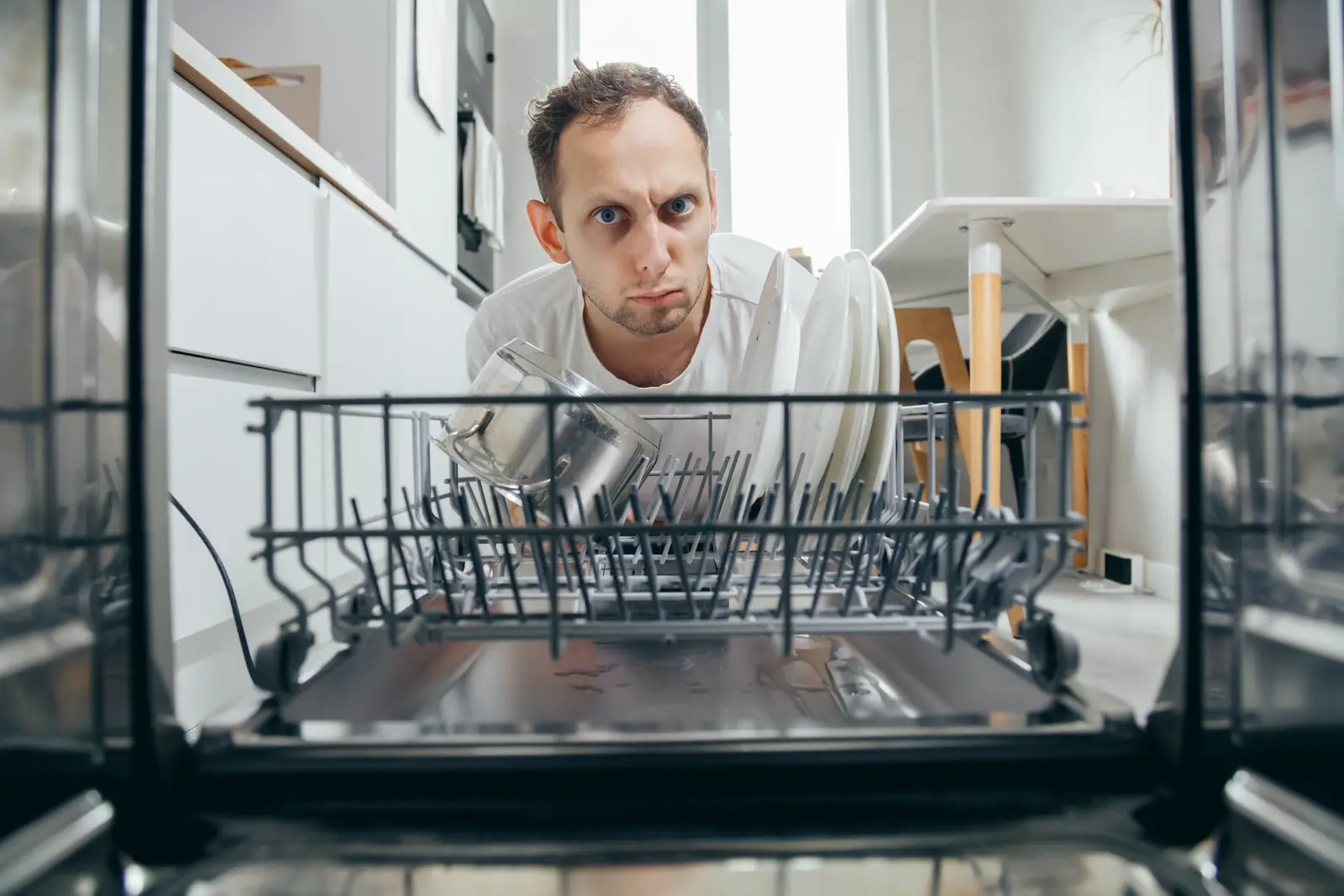 Man staring into an open dishwasher in a modern kitchen — checking why dishes have not been cleaned properly