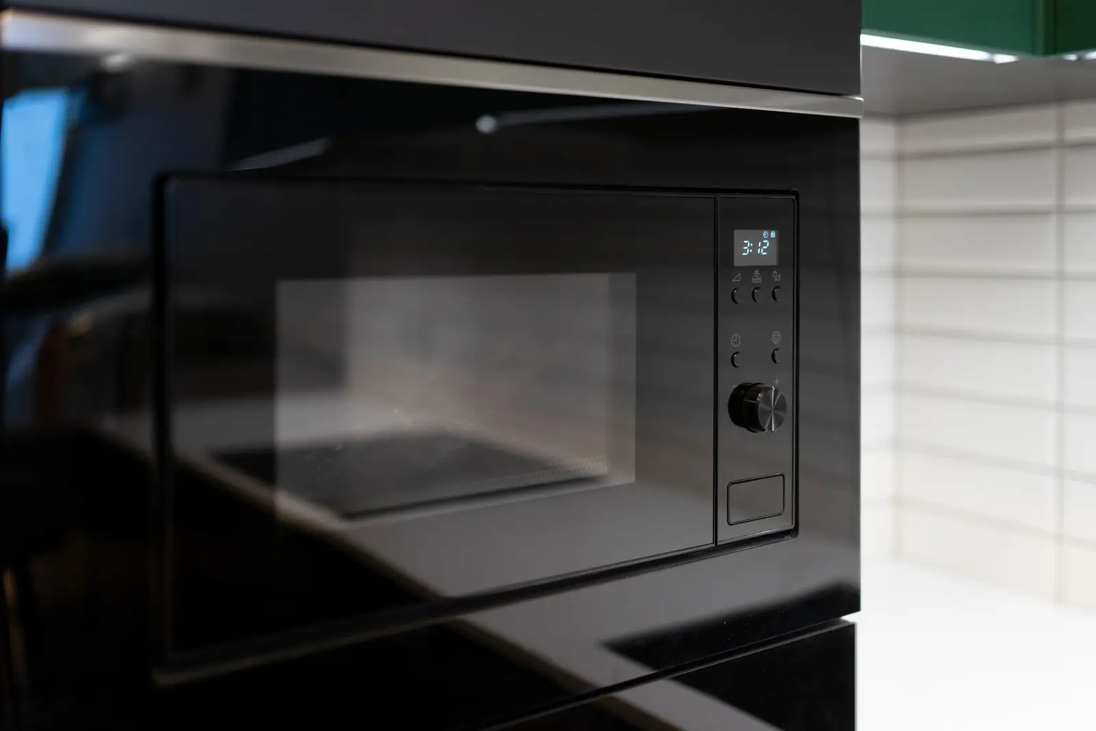 Modern black integrated microwave oven set into white tiled kitchen cabinetry — built-in models create a seamless, purpose-built appearance