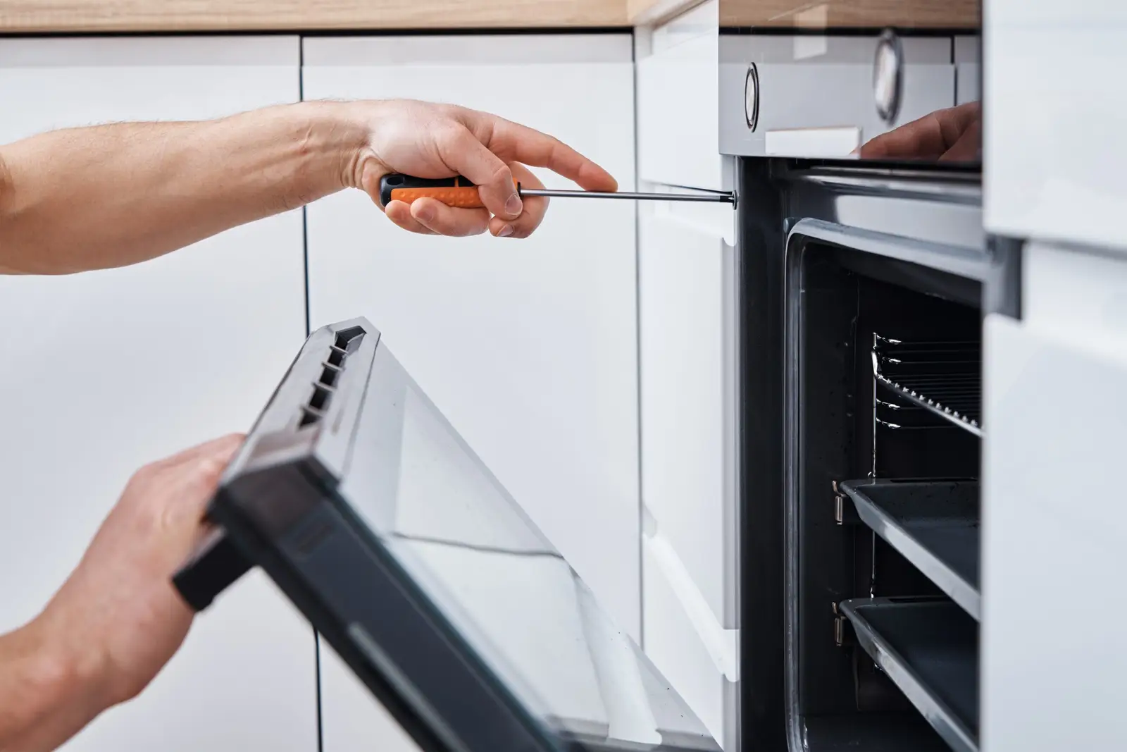 Adult using a screwdriver to repair a built-in oven — electrical and component faults require a qualified engineer