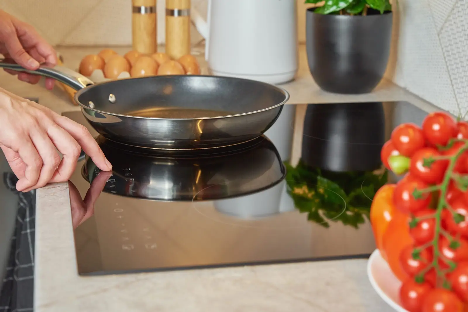 Woman turning on an induction hob with a frying pan — pan choice has the biggest influence on how much noise an induction hob produces