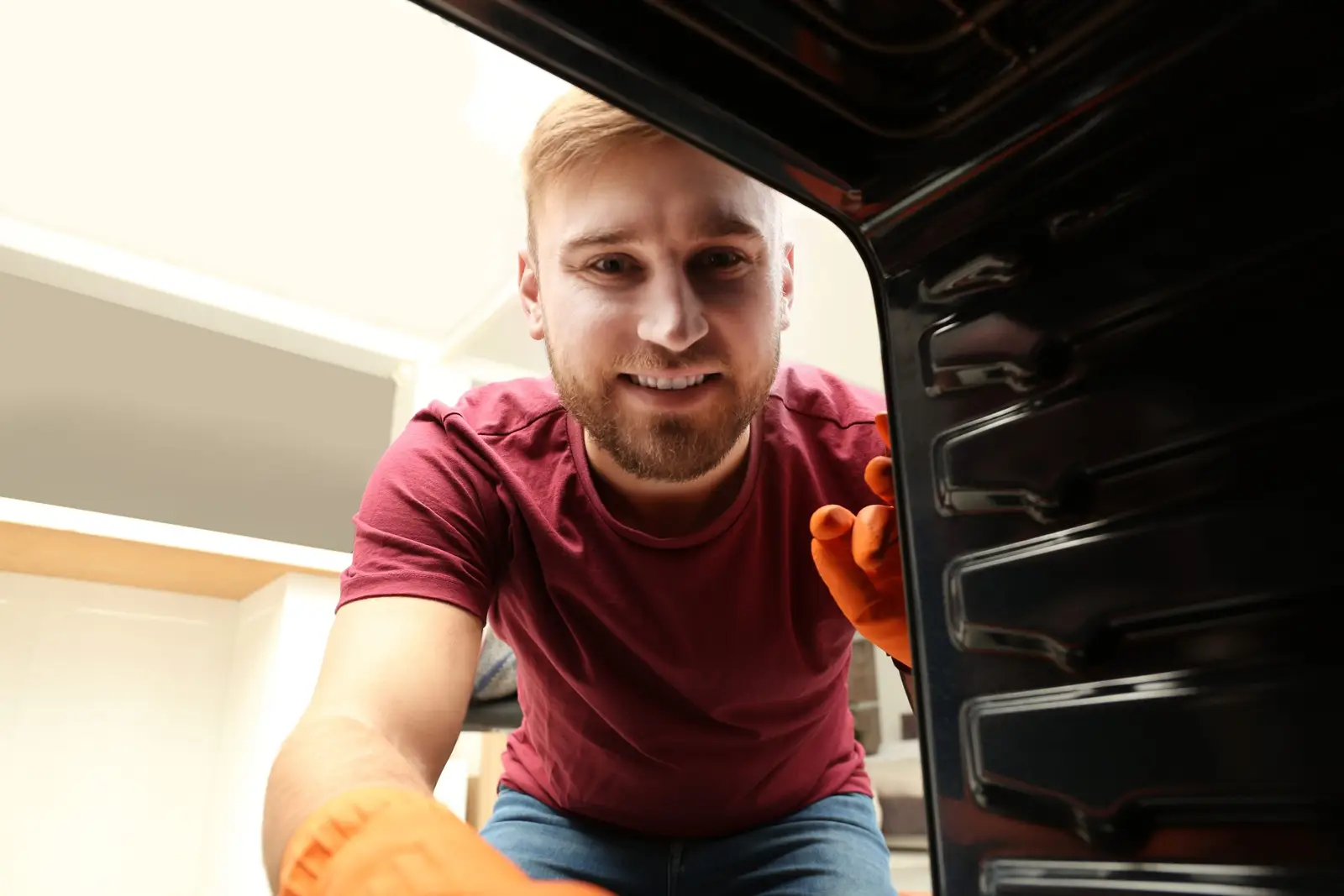 Young man cleaning the interior of a built-in oven — many common oven problems can be resolved with simple checks before calling an engineer