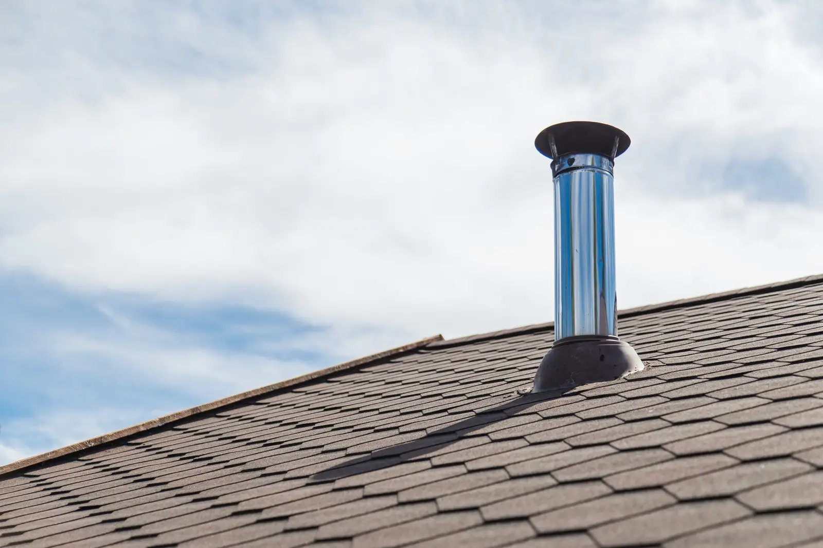 Brick chimney on a house rooftop against a blue cloudy sky